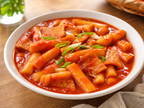 Sagua tteokbokki in spicy red sauce served in ceramic bowl on wooden table