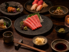 Omakase table setting with chutoro sashimi, soy sauce, wasabi, sake cup and chopsticks on dark wood