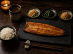 Korean fine dining table setting with grilled eel, steamed rice, banchan side dishes and barley tea on dark wood