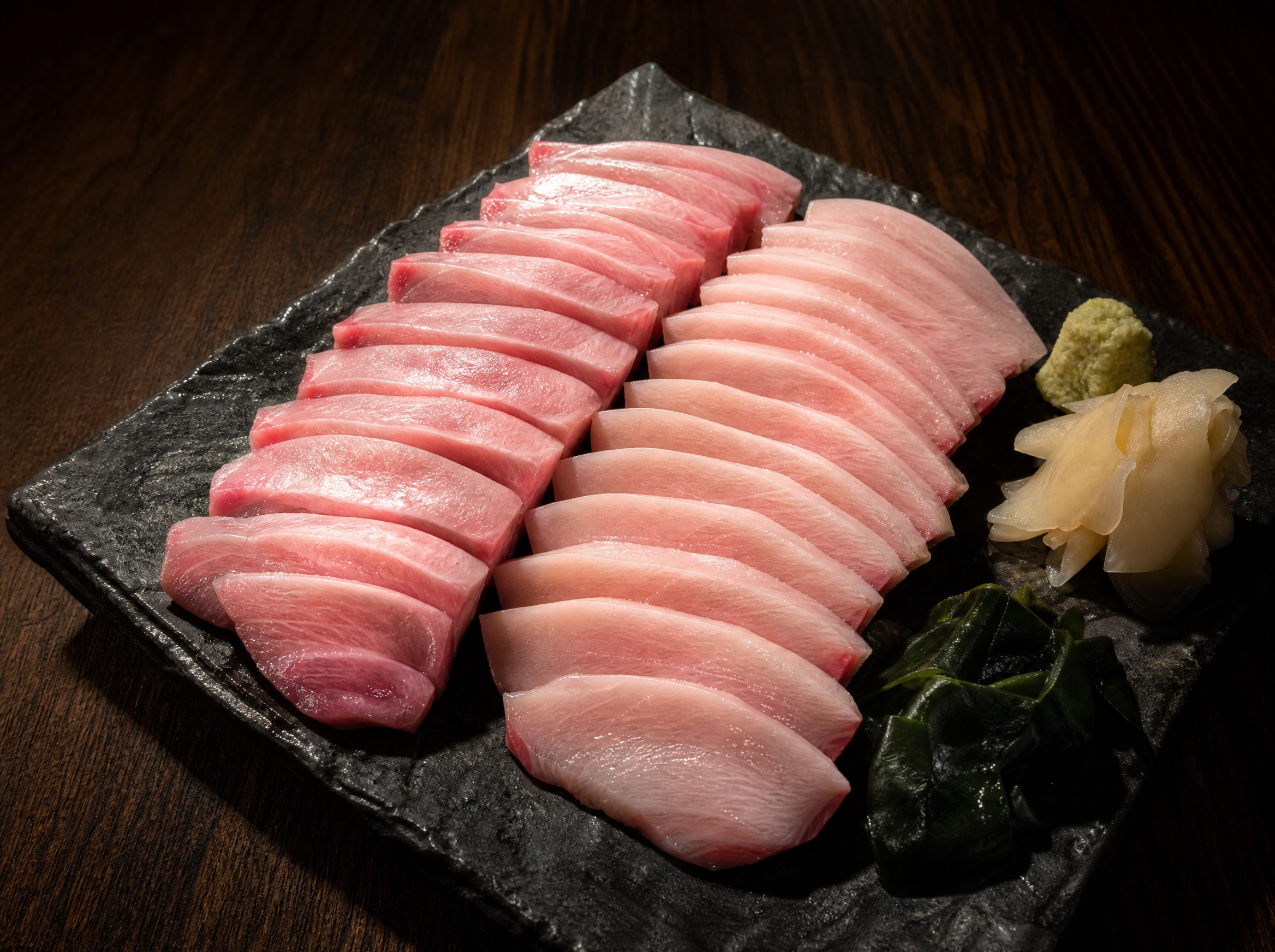 Premium yellowtail hamachi sashimi set with belly and loin cuts, gamtae seaweed, wasabi and pickled ginger on dark slate