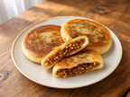 Korean hotteok sweet pancakes golden-brown on ceramic plate, one split open showing honey-nut filling, bright wooden table