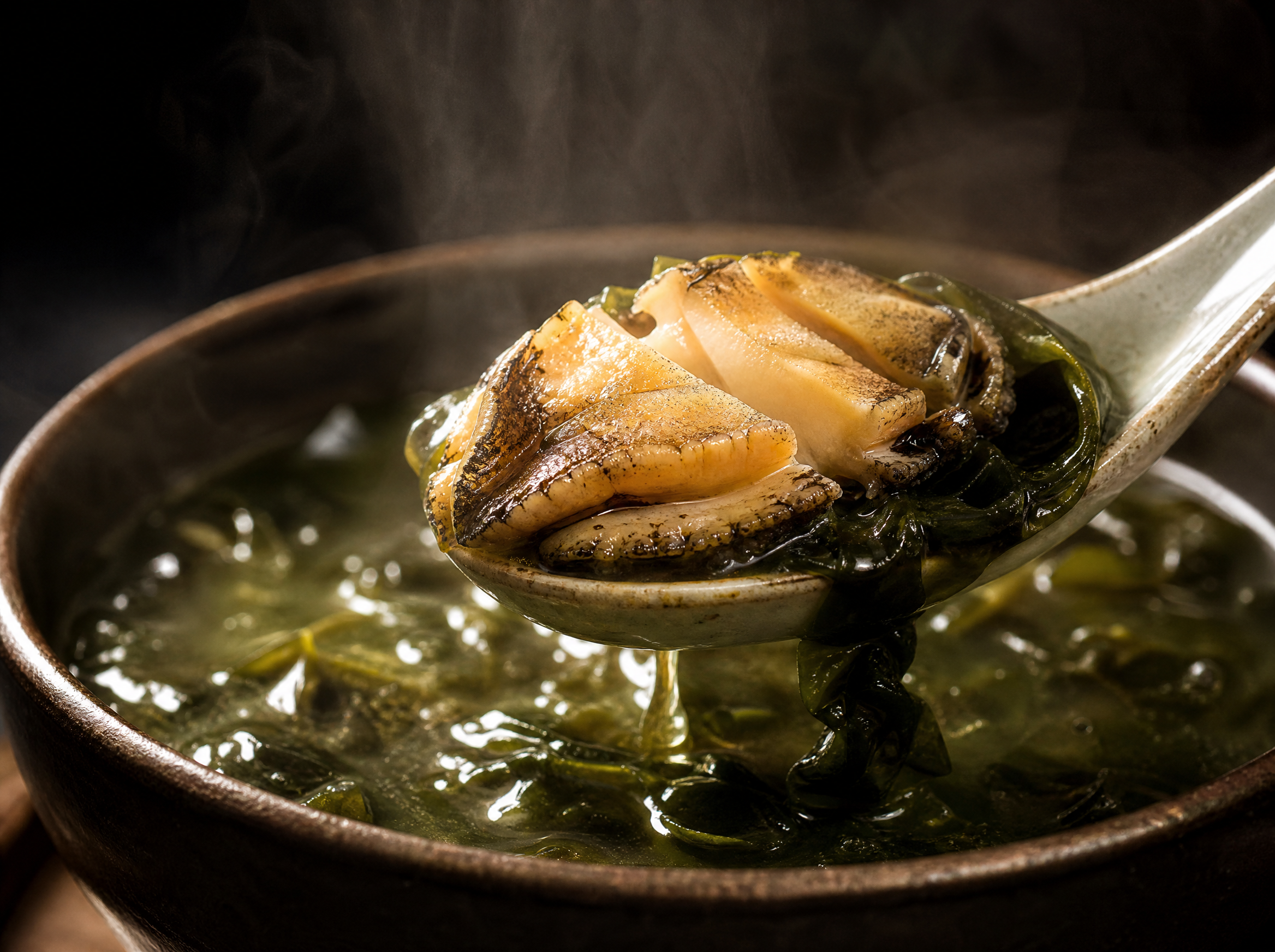 Macro close-up of abalone seaweed soup with abalone piece being lifted by ceramic spoon from rich broth