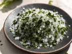 Macro close-up of premium sea salt crystals and dark green gamtae seaweed flakes on dark ceramic dish showing mineral texture