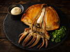 Korean grilled whole cuttlefish gapojingeo-gui on dark slate plate with tentacles fanned out, green onion and mayo dipping sauce