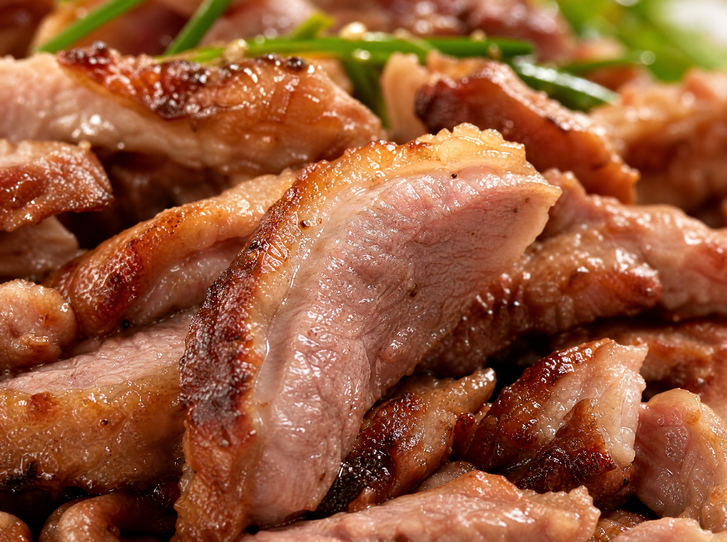 Macro close-up of Korean grilled duck slices showing crispy caramelized exterior and juicy interior with glistening duck fat