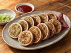 Gangneung squid sundae sliced rounds on ceramic plate with gochujang sauce, bright wooden table