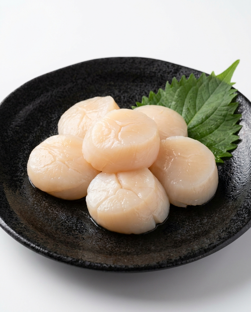Raw sashimi-grade Hotate scallops on a black ceramic plate with shiso leaf